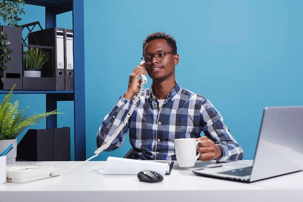 Jeune homme d'affaires adulte parlant sur un téléphone fixe dans l'espace de travail du bureau de l'agence de création. Chef d'équipe du département de développement en conversation téléphonique avec un représentant des travailleurs parlant d'un projet de démarrage.