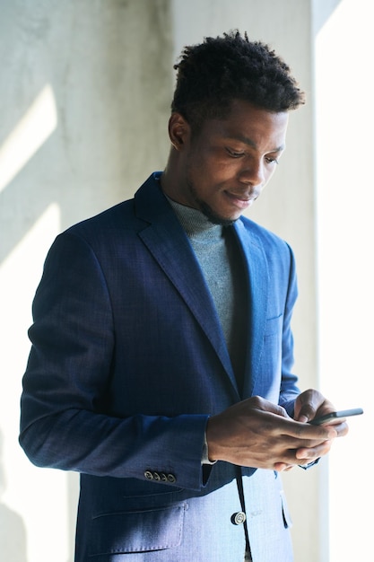 Jeune homme d'affaires afro-américain sérieux en tenues de soirée utilisant un téléphone portable