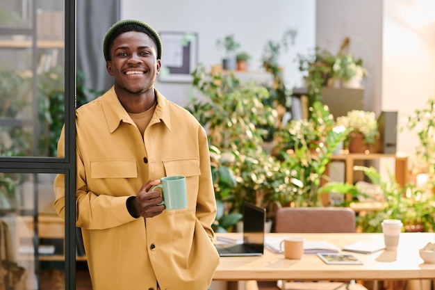 Jeune homme d'affaires afro-américain souriant avec une tasse de thé ou de café