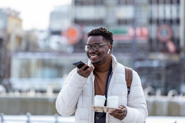 Photo jeune homme d'affaires afro-américain tenant du café dans une tasse en carton et parlant au téléphone