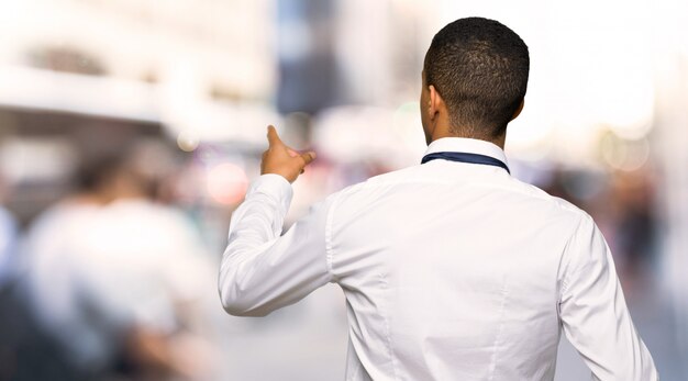 Jeune homme d'affaires américain afro pointant vers l'arrière avec l'index de la ville