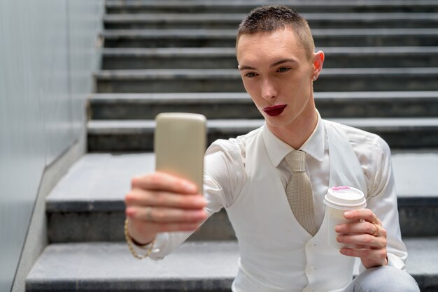 Jeune homme d'affaires androgyne prenant selfie avec téléphone