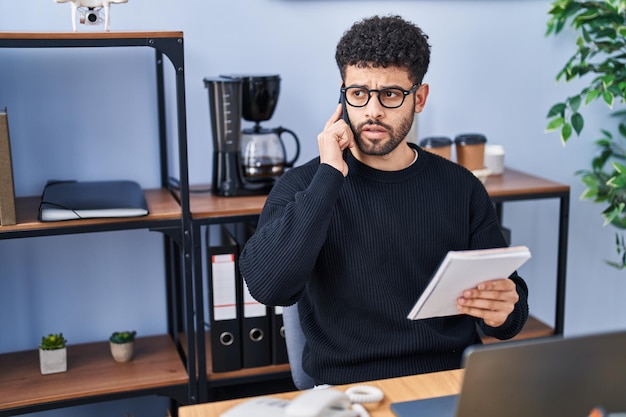 Jeune homme d'affaires arabe parlant sur le smartphone lisant un cahier au bureau