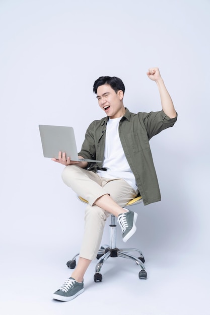 Jeune homme d'affaires asiatique assis sur une chaise et utilisant un ordinateur portable en arrière-plan