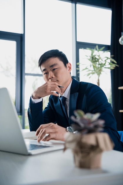 Jeune homme d'affaires asiatique concentré travaillant avec un ordinateur portable