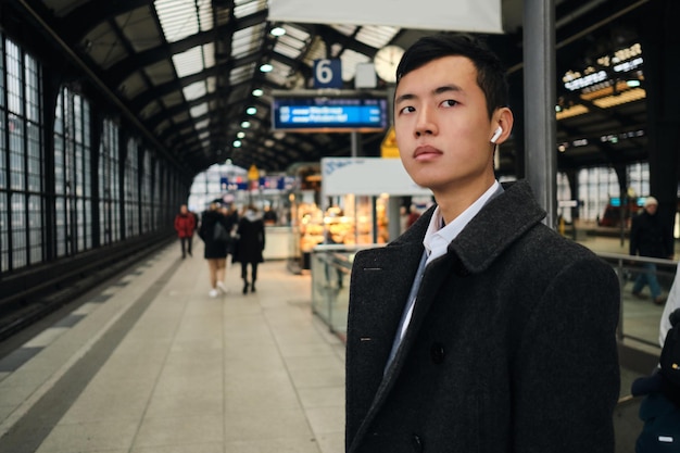 Jeune homme d'affaires asiatique confiant dans des écouteurs sans fil attendant le train à la station de métro