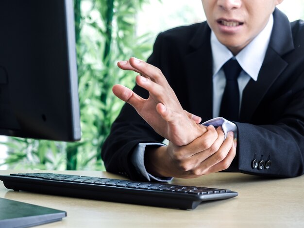 Jeune homme d'affaires asiatique en costume obtenant des douleurs à la main lors de l'utilisation d'un ordinateur portable au bureau