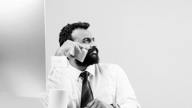 Jeune homme d'affaires asiatique indien en barbe occupé à un appel téléphonique tout en utilisant un ordinateur portable ou un ordinateur au bureau