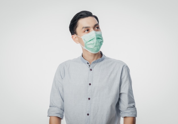 Jeune homme d'affaires asiatique portant un masque hygiénique et levant pour prévenir l'infection, 2019-nCoV ou coronavirus. Maladies respiratoires aéroportées telles que les combats du PM 2,5 et la grippe isolée sur un mur blanc