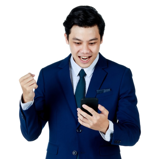 Jeune homme d'affaires asiatique séduisant portant un costume bleu marine avec une chemise blanche et une cravate vérifiant son téléphone portable et célébrant sur fond blanc. Isolé