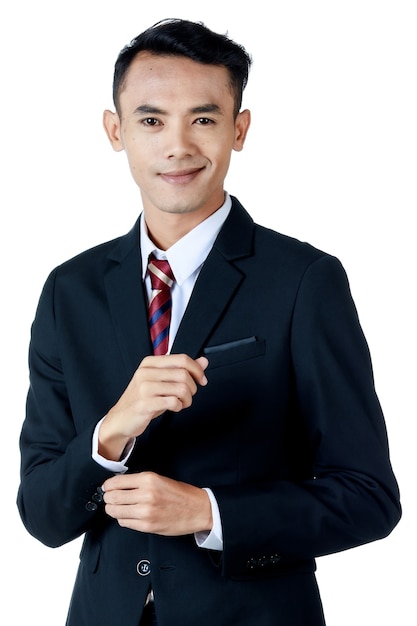 Jeune homme d'affaires asiatique séduisant portant un costume noir avec une chemise blanche et une cravate souriant et boutonnant sa manche sur fond blanc. Isolé