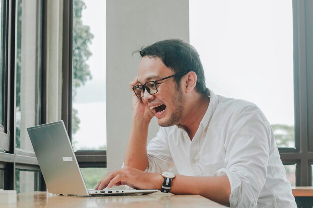 Jeune homme d'affaires asiatique souriant tout en travaillant sur un ordinateur portable au bureau à domicile