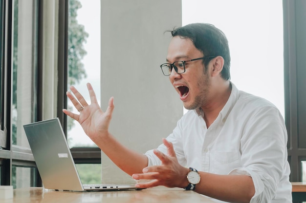 Jeune homme d'affaires asiatique souriant tout en travaillant sur un ordinateur portable au bureau à domicile