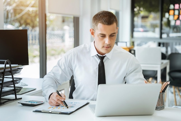 Jeune homme d'affaires asiatique travaillant au bureau avec un ordinateur portable et des documents sur la table