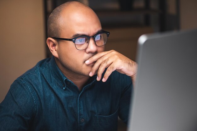 Jeune homme d'affaires asiatique travaillant avec un ordinateur dans le bureau sombre la nuit