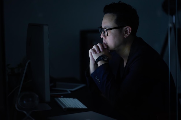 Jeune homme d'affaires asiatique travaillant sur un ordinateur portable tout en regardant l'ordinateur à son bureau la nuit