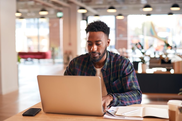 Jeune homme d'affaires assis au bureau avec ordinateur portable dans un bureau à aire ouverte moderne