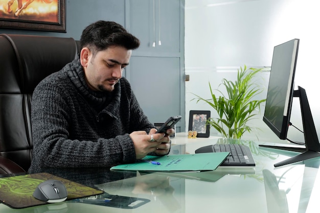 Un jeune homme d'affaires assis au bureau et utilisant son téléphone portable.