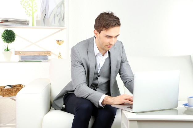 Jeune homme d'affaires assis sur un canapé et utilisant un ordinateur portable à la maison