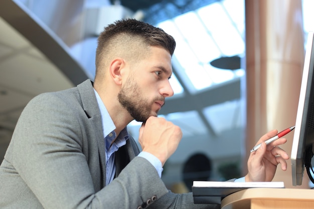 Jeune homme d'affaires assis et regardant un écran d'ordinateur tout en travaillant au bureau