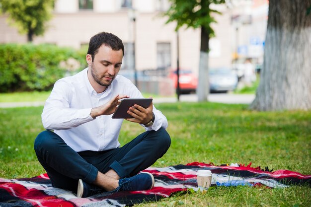 Jeune homme d'affaires au parc travaillant avec tablette