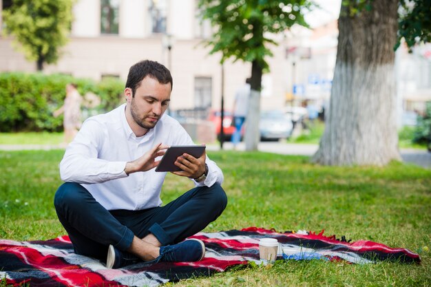 Jeune homme d'affaires au parc travaillant avec tablette