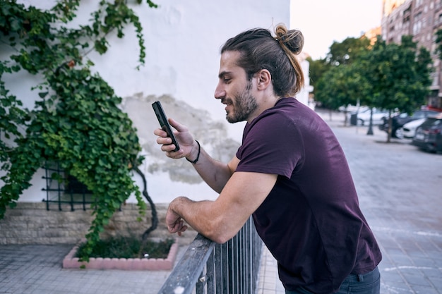 Jeune homme d'affaires aux cheveux longs à l'aide de son téléphone dans la rue