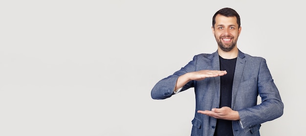 Jeune homme d'affaires avec une barbe dans une veste, faisant des gestes avec ses mains montrant un signe de grande et grande taille un symbole de mesure.