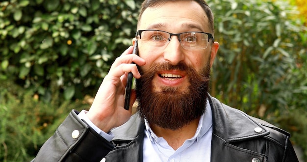 Photo jeune homme d'affaires barbu parlant sur son téléphone à l'extérieur.