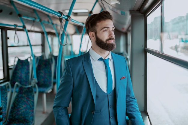 Jeune Homme D'affaires Barbu Réfléchi En Costume Bleu, Debout Dans Les Transports Publics Et à La Recherche De La Fenêtre De L'auge.