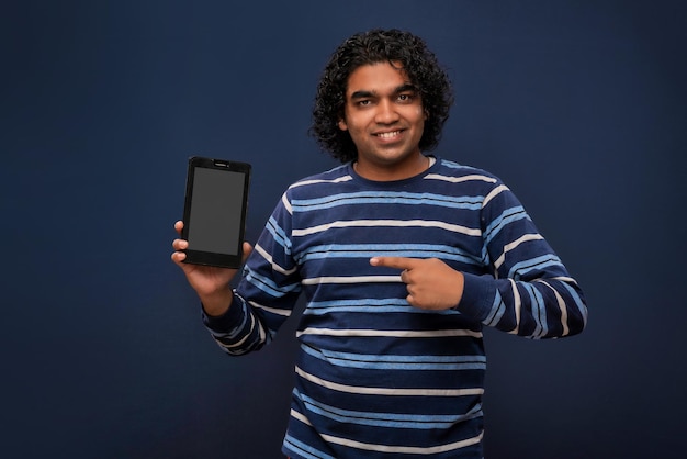 Jeune homme d'affaires beau jeune homme montrant un écran vide de smartphone ou de téléphone portable ou de tablette sur fond gris
