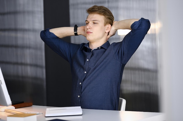 Jeune homme d'affaires blond et programmeur qui s'étire les mains après avoir travaillé dur avec l'ordinateur. Une entreprise en démarrage mène au succès.