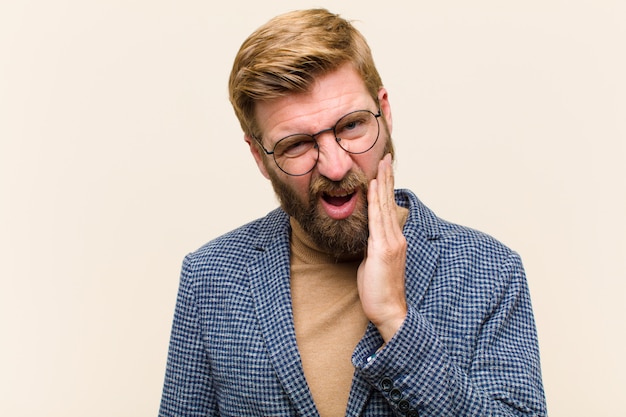 Jeune homme d'affaires blond tenant la joue et souffrant de maux de dents douloureux, se sentir malade, misérable et malheureux, à la recherche d'un dentiste