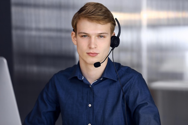 Jeune homme d'affaires blond utilisant un casque et un ordinateur au travail. Une entreprise en démarrage signifie travailler dur et hors du temps pour réussir.