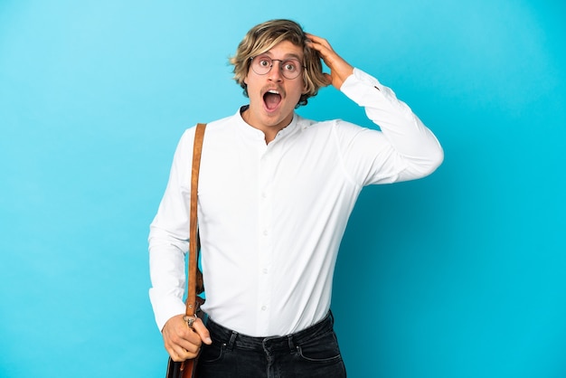 Jeune homme d'affaires blonde isolé sur bleu avec une expression de surprise