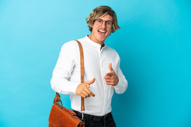 Jeune homme d'affaires blonde isolé sur un mur bleu pointant vers l'avant et souriant