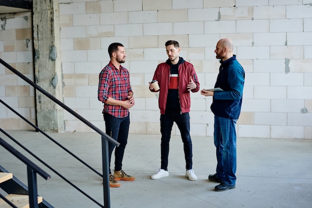 Jeune homme d'affaires avec boisson expliquant son point de travail tout en regardant l'un de ses collègues pendant le brainstorming et la discussion d'idées