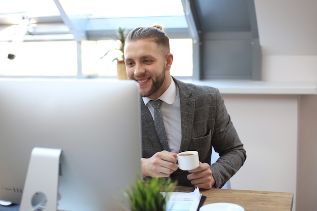 Jeune homme d'affaires buvant du café au bureau en tapant sur l'ordinateur.