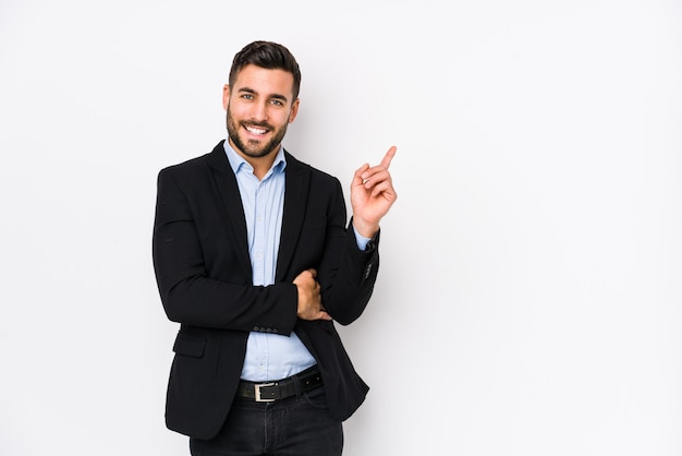 Jeune homme d'affaires caucasien contre un mur blanc souriant joyeusement pointant avec l'index loin.