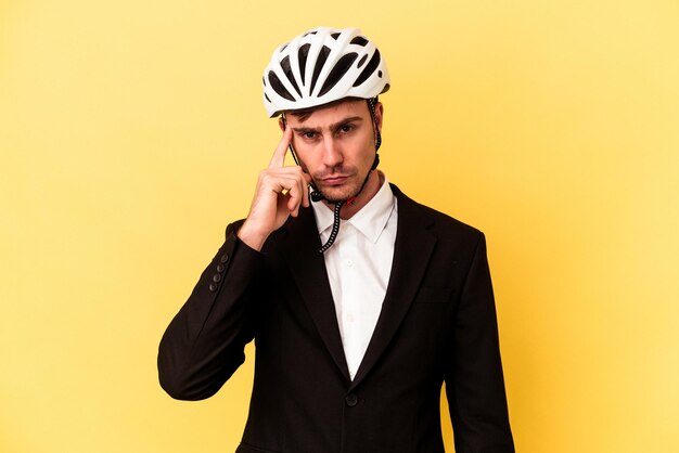 Jeune homme d'affaires caucasien portant un casque de vélo isolé sur fond jaune pointant le temple avec le doigt, pensant, concentré sur une tâche.