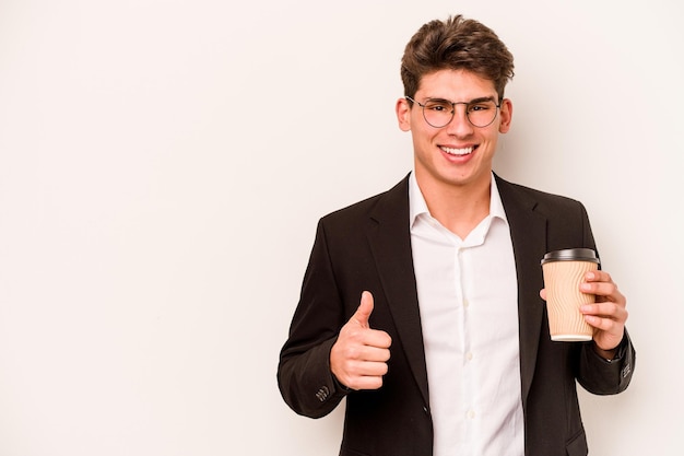 Jeune homme d'affaires caucasien tenant du café à emporter isolé sur fond blanc souriant et levant le pouce vers le haut