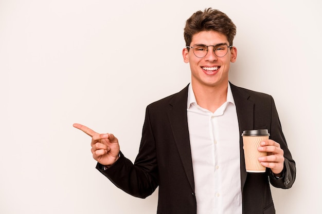 Jeune homme d'affaires caucasien tenant du café à emporter isolé sur fond blanc souriant et pointant de côté montrant quelque chose à l'espace vide