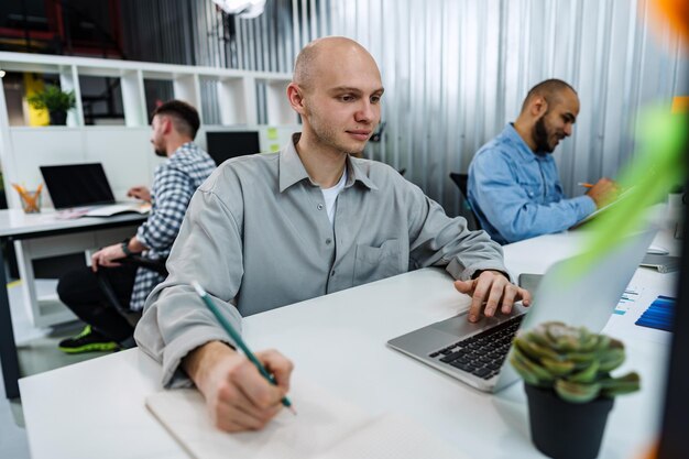 Jeune homme d'affaires chauve assis au bureau au bureau travaillant sur ordinateur