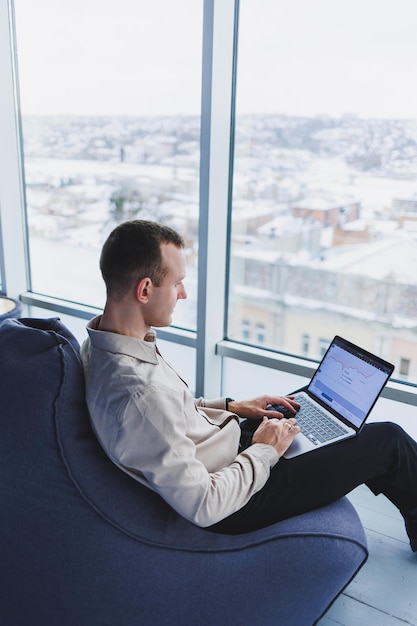 Jeune homme d'affaires concentré regardant des informations sur l'écran d'un ordinateur portable en ligne ou travaillant à distance en ligne au bureau à domicile communiquant à distance avec le client ou l'étude