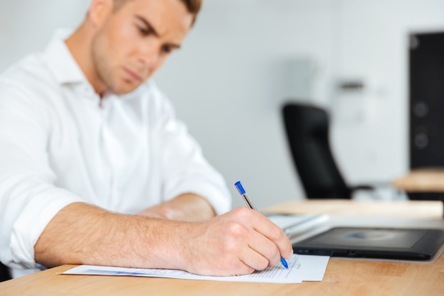 Jeune homme d'affaires concentré s'asseyant et écrivant à la table