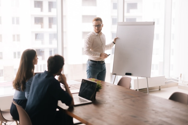 Jeune homme d'affaires confiant présentant un nouveau projet aux partenaires sur tableau blanc