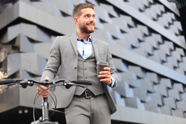 Jeune homme d'affaires confiant avec son vélo buvant du café à l'extérieur.