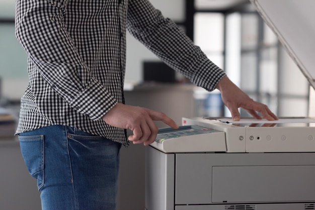 jeune homme d'affaires copie des documents sur une photocopieuse à l'intérieur du bureau de démarrage moderne, vêtements décontractés