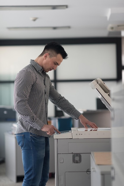 jeune homme d'affaires copie des documents sur une photocopieuse à l'intérieur du bureau de démarrage moderne, vêtements décontractés