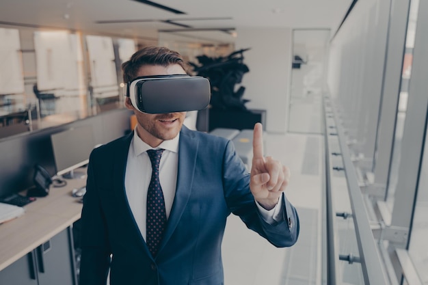 Jeune homme d'affaires en costume élégant utilisant un casque vr touchant l'exploration de la réalité virtuelle au travail